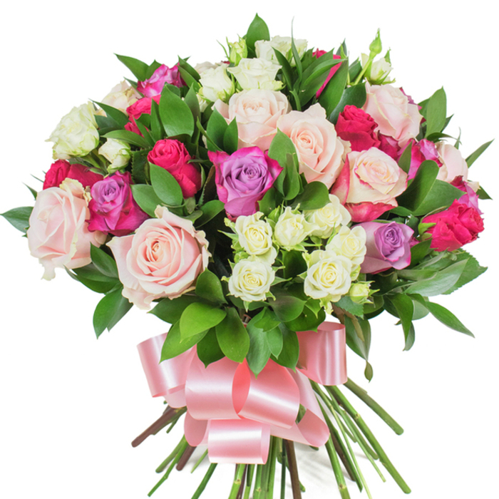 A sumptuous, rounded bouquet of mixed roses is photographed against a bright white backdrop, its dense composition emphasising colour, texture, and floral craftsmanship. Dominant are large roses in tender pastel pink and creamy white; some open fully to reveal concentric petals with silky edges, others remain in neat bud form to add structural interest. Brighter magenta-pink roses are placed to create striking focal points, while delicate lavender roses offer gentle cool tones that balance the warmer shades. Interspersed among these are abundant clusters of small spray roses-mostly pristine white with hints of pale yellow at their cores-introducing a fine, dotted texture that softens the arrangement's mass. Lush, dark green foliage-appearing as ruscus or salal-provides a glossy, supportive framework, its elongated leaves tucked between blooms to accentuate depth and silhouette. The stems below are gathered and bound with a wide, baby-pink satin ribbon tied into an elegant bow; the ribbon's sheen echoes the roses' soft glow and signals the bouquet's celebratory purpose. Under neutral studio light the colours read true and vibrant, making this composition ideal for occasions that call for heartfelt sentiment and refined beauty-Valentine's Day, birthdays, anniversaries, or a thoughtful Mother's Day delivery. As a local florist accustomed to serving Queensbury and surrounding NW London streets, I can picture this arrangement arriving at doorsteps off Kingsbury Road or brightening a kitchen table near local parks, carrying both floral freshness and considered design.