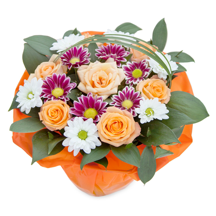 A lush, thoughtfully composed bouquet bursts with colour and life, photographed from a softly elevated top-down angle to reveal the full tapestry of its blooms. Central to the design are peach and orange roses, their classic, layered petals gradually opening to display opulence and warmth. These focal blooms are interspersed with delicate clusters of white chrysanthemums-each daisy-like flower boasting bright white petals and dew-kissed green centers, providing a clean, invigorating freshness reminiscent of Queensbury's green spaces. Adding drama and a sense of playful luxury, magenta and deep purple chrysanthemums, with their finely textured petals and vibrant lime discs, bring a rich contrast that energises the entire composition. The bouquet is enveloped by glossy, dark green foliage, likely ruscus, whose broad leaves weave in and out, adding structure, colour, and a sense of grounded plentifulness akin to the area's gardens and tree-lined avenues. A striking arc of decorative bear grass curves gracefully over the bouquet, creating movement and a nod to contemporary floristry trends. At the base, vivid orange cellophane is folded and crinkled, gathering the arrangement securely and highlighting the warm tones above-an inviting gesture for celebrations or as a unique table centrepiece. This expertly crafted floral gift is perfect for evoking joy, gratitude, or admiration and stands as a testament to the skilled artistry and fresh local blooms available in Queensbury, ideal for thoughtful gestures and memorable occasions alike.
