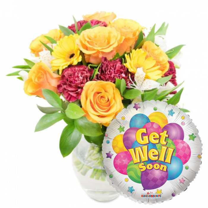 A warm, hopeful 'Get Well Soon' composition that reads like a well-crafted care package from a neighbourhood florist in Queensbury, arranged with attention to colour, scent and balance. The bouquet is abundant, set in a simple clear glass vase so the stems and water are visible, and features several large, half-open roses in sunny orange and deep yellow hues whose layered petals catch the light and offer a gentle fragrance. Intermingled are bright yellow gerbera daisies, their cheerful disc-shaped blooms bringing an open, sunny energy, and deep burgundy carnations whose ruffled, velvety textures provide dimensional contrast. Small white alstroemeria punctuate the mass of colour, introducing lightness and delicate linear accents among the rounder shapes. Lush green foliage frames the arrangement and breathes freshness into the composition, creating an impression of a garden-picked bouquet ready to brighten a bedside table. To the lower right, overlapping the flowers, a reflective silver Mylar balloon stands out: its border dotted with small stars, and its centre showing a playful cluster of cartoon balloons in blue, purple, pink, yellow and green with patterned details. The message Get Well Soon is presented in bold yellow-and-blue lettering with a slight shadow, and a tiny 'KALEIDOSCOPE' logo appears near the balloon's bottom rim. As a local florist familiar with deliveries across Queensbury, Kingsbury and nearby Wembley, I see this pairing as a considerate, uplifting choice-colourful, textural and scented-to send to someone healing at home or recovering in hospital.