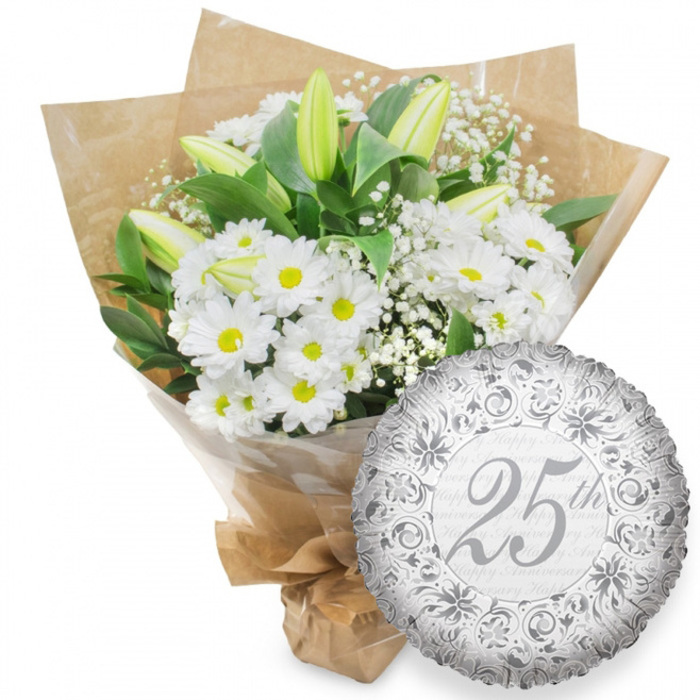 A refined anniversary arrangement is presented as if ready to be delivered to a doorstep in Queensbury, its simple white background ensuring every detail of the bouquet and balloon stands out. On the left, a generous cluster of white daisy chrysanthemums fills the frame, their petals forming neat circles around warm yellow centres that suggest gentle happiness rather than loud celebration. Threaded through this cushion of blooms are slender stems of white lilies, still in bud, their elongated forms adding height and anticipation. The tips of the lily buds show a delicate green flush, hinting at their freshness and the subtle fragrance that will emerge as they open over the next days. Fine sprays of white gypsophila drift between the larger flowers like tiny stars, softening edges and making the bouquet feel cloud-like and romantic. Dark green leaves, polished and sturdy, peek out from behind the flowers, grounding the design. The whole arrangement is wrapped in a clear cellophane sleeve that catches small reflections of light, then embraced by rustic brown kraft paper folded into a wide collar, the natural paper giving the bouquet an earthy, contemporary look you might see in a stylish Queensbury café window. The stems are gathered and tied neatly at the base, ready for gifting. To the lower right, a round silver foil balloon adds a distinctly festive note. Its metallic surface is patterned with swirling scrolls and delicate floral flourishes in deeper silver, while the centre displays a large, elegant 25th in script. Behind the main text, the words Happy Anniversary repeat softly, reinforcing that this is a special Silver Anniversary gift designed to honour a lasting partnership.