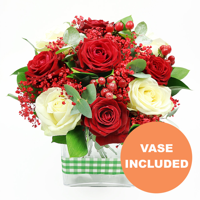 A carefully composed red and white rose arrangement is photographed against a clean, white background, every petal and leaf clearly defined, as if you are standing right beside it in a Queensbury florist studio. At the centre, generous clusters of deep red roses take pride of place, their velvety petals curling outward in rich, layered whorls that convey romance and celebration. Interspersed among them, creamy white roses with smooth, gently opening blooms bring light to the design, creating a graceful contrast that softens the intense reds. Woven throughout the bouquet are fine sprays of tiny red filler flowers that resemble dyed baby's breath, their many small blossoms forming a delicate, cloud-like texture that fills the gaps between the larger heads. Dotted between these, shiny red hypericum berries appear in rounded bunches, their glossy skins catching highlights and adding dimension and festive energy. The greenery is thoughtfully arranged, with deep green leaves giving fullness at the base and silvery-green eucalyptus stems peeking through, their rounded leaves introducing a cool, modern accent that feels right at home in stylish Queensbury apartments or family houses near the tube station. All the stems are gathered neatly into a contemporary, clear rectangular glass vase, allowing you to see the straight, carefully trimmed stems and the water line within. Around the centre of the vase, a green and white gingham ribbon is wrapped in a neat band, its checked pattern evoking a cosy, rustic tablecloth and adding a playful, homely touch. In the lower right corner of the image, an orange circular graphic with bold white text reads VASE INCLUDED, clearly indicating that this is a complete, ready-to-display gift-ideal for anniversaries, Valentine's surprises, or simply brightening a living room in Queensbury with fresh, professionally arranged flowers.