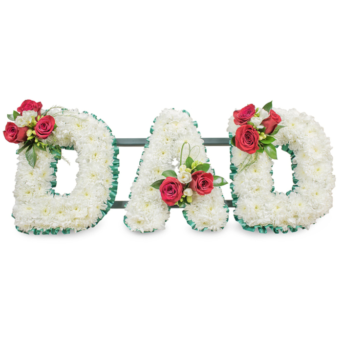 A thoughtful and dignified sympathy statement spells DAD in three substantial floral letters, each densely covered with pure white chrysanthemum blooms to form a uniformly soft, textured surface that feels both reverent and composed. The letters are crisply edged in a deep emerald green pleated ribbon that outlines each curve and angle with tidy precision, lending a tailored, almost architectural finish to the organic mass of flowers. Carefully positioned accent clusters punctuate the design: on the upper left curve of the first D a compact spray of rich red roses-their petals lush and velvety-intermingles with small white freesia and glossy foliage; the A features a corresponding grouping near the base of its left stem, accented by slender, looping strands of bright green bear grass that introduce a subtle, modern line; the final D mirrors the first, creating a balanced three-point composition. Slightly visible behind the blooms are narrow dark support bars which hold the letters together for display at a funeral venue. The overall palette-crisp white, deep red and vivid green-reads both pure and warm, and if one could smell the tribute it would carry the soft sweetness of freesia with the deeper rose scent folded into fresh green leaves. Crafted with the care of a local florist familiar with ceremonies in Queensbury, Harrow and nearby Wembley, this bespoke funeral piece is designed to convey sincere love, respect and remembrance for a father or paternal figure.