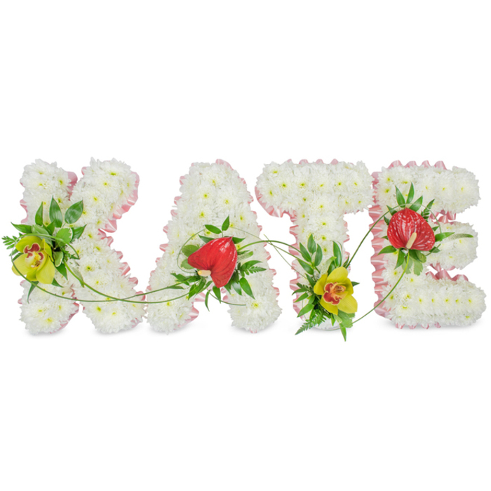 Shown against a plain, light background, this bespoke funeral flower arrangement spells the name KATE in four bold, carefully shaped letters. Each capital letter is generously filled with flawless white chrysanthemums, packed closely to create a deeply textured, cushion-like surface that feels gentle to the eye and symbolises purity, remembrance, and peace. The outer edges of every letter are outlined with a softly gathered pink ribbon trim, its satin sheen catching the light and lending a subtle, feminine warmth to the tribute. Rather than remaining purely white, the design is thoughtfully accented with vivid feature blooms placed at key points. On the left side of the K and nestled at the lower curve of the T, green cymbidium orchids with warm reddish centres stand out, their exotic star-like petals and sturdy stems bringing a note of quiet strength and sophistication. On the A and the E, glossy red anthuriums shaped like small hearts offer a bold contrast, their rich colour and waxy texture hinting at enduring love amid sorrow. These standout flowers are cradled by lush greenery, including broad dark leaves and airy sprigs of fern that add depth and natural movement. Slim green tendrils arc and thread gently from one letter to the next, visually joining the name and suggesting the unbroken connection between memories and those left behind. Created in the style of a skilled Queensbury florist familiar with local funeral traditions, this KATE tribute would be placed alongside other sympathy flowers at a service, wake, or graveside gathering in the Queensbury area, offering a deeply personal and heartfelt final gesture.