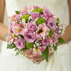 The scene unfolds in Queensbury, where a delicate bridal bouquet is brought to life with the artful hands of experienced local florists. Held gently at the outset of a wedding ceremony, the bouquet's soft contours and layered textures immediately draw the eye. Tightly arranged roses, their colors ranging from the softest blush pink to gentle lavender purple, anchor the bouquet; their petals delicately dewy and velvety, offering whispers of scent that mingle with the promise of a joyful union. Alternating with the roses, button chrysanthemums in lively lime green provide a playful textural counterpoint, their round forms echoing the spherical shape of the bouquet and adding a crisp modernity. Alstroemeria blooms, with intricate pink petals streaked with maroon and lemon-yellow, peek out among the lush greenery, lending an exotic and refined touch. Airy clusters of baby's breath drift throughout the design-each tiny white floret a miniature celebration, framing the fuller blossoms with a gauzy beauty. Deep green leaves offer a sturdy, natural stage for the pastel colors, their subtle gloss whispering of freshness found in Queensbury parks on a spring morning. The overall effect is both tranquil and vibrant, reflecting the joyous spirit of local weddings. This bouquet, a symphony of colour and form, speaks to commitments celebrated across Queensbury, perfectly embodying both romantic tradition and creative floral artistry-an inspiring visual for any story focused on contemporary bridal flowers or unforgettable wedding details.