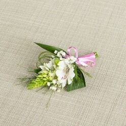An elegant floral buttonhole is laid carefully on a pale beige, linen-like cloth, the subtle weave of the fabric giving a warm, natural backdrop that enhances the freshness of the blooms. The focal point is a single white alstroemeria flower, fully open, with smooth, slightly ruffled petals that curl softly at the tips. Near the throat of the bloom, fine reddish-brown streaks and speckles draw the eye inward, giving the blossom an intricate, almost hand-painted character. To one side, a compact, cone-shaped cluster of vivid green buds, similar to Ornithogalum, rises like a miniature spire, its tightly layered structure offering a bold contrast to the softness of the alstroemeria. Around these focal elements, airy sprays of white baby's breath create a delicate halo, each tiny blossom catching the gentle, even lighting and contributing to a sense of lightness and romance. Supporting foliage in rich, deep greens frames the flowers: broad, pointed leaves provide a steady base, while slender, flexible grass-like fronds stretch and curl, adding texture and dynamic lines to the arrangement. A bright pink satin ribbon, tied into a crisp, small bow at the right, gathers the stems and introduces a playful note of colour without overwhelming the calm palette of whites and greens. This handcrafted boutonniere feels ideal for weddings and proms in Queensbury, the sort of detail a local florist from Flower Delivery Queensbury would design for a lapel on a summer afternoon, bringing a quiet, polished beauty to formal attire during celebrations around the high street or nearby parks.