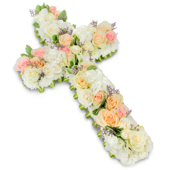 A beautifully detailed floral cross is presented on a pure white backdrop, every inch of its surface covered in tender, pastel blooms that create a sense of quiet reverence. The cross itself is rounded and softly contoured, built from a dense foundation of white and creamy ivory flowers. Large, fully open roses sit beside smaller spray roses, their petals forming intricate rosettes that give the arrangement a rich, layered texture. Between these, clusters of fluffy white hydrangea or chrysanthemum-style blooms fill any gaps, so the cross appears luxuriously full, like a cushioned bed of petals. Woven throughout the white base, gentle tones of pale peach, apricot, and light blush pink roses provide warmth and emotional depth. These pastel accents run through the centre and arms of the cross in thoughtfully placed clusters, suggesting cherished memories and tender farewells. Scattered here and there, you can notice tiny flecks of lavender or pale purple filler flowers, which add an almost whispered hint of colour and further intricacy without overwhelming the soft palette. Slim tendrils and small leaves of fresh green foliage emerge at the edges, outlining the cross and adding natural definition. The lighting is bright yet calm, emphasising each curve, petal, and shadow, and giving the piece a polished, professional appearance. Crafted with the care you'd expect from a local Queensbury florist who understands the sensitivity of funeral and memorial tributes, this floral cross feels perfectly suited for services in nearby chapels or funeral homes, offering a message of peace, faith, and enduring love to grieving families.