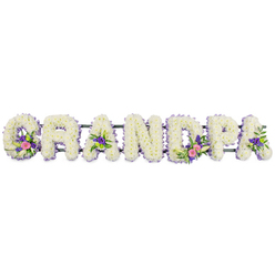 A carefully composed funeral name tribute spells out GRANDPA in seven bold, floral letters, set against a smooth white backdrop that highlights each nuance of colour and texture. Every character is formed from a dense bed of small white chrysanthemums or similar blossoms, their tightly layered petals creating a velvety, cloud-like surface that suggests gentleness and peace. Around the outside edge of each letter, a narrow border of dainty lilac and purple flowers runs like a soft ribbon, giving structure and a cool, tranquil glow. Within selected letters-the 'G', the first 'A', the 'D', and the final 'A'-small posies of accent blooms are nestled into the white, including graceful white lily forms, pink and fuchsia petals, and vivid purple florets. Bright green button chrysanthemums and rich green leaves are woven through these pockets of colour, adding movement and a sense of fresh life. The letters are supported on a slim, dark green bar that is just visible behind them, aligning the word so it could rest beautifully at the head of a coffin or by a graveside in Queensbury Cemetery or a local chapel of rest. The overall feeling is one of quiet sincerity, like a gentle farewell spoken in flowers from grandchildren who grew up around Queensbury station and the nearby streets. Though still and composed, this tribute conveys warmth, gratitude, and lasting love for a grandfather, reflecting the kind of thoughtful design a Queensbury florist would prepare for a family seeking comfort and dignity at a time of loss.
