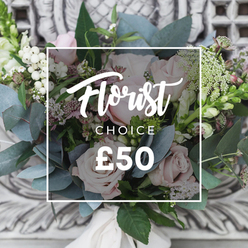 There is a quiet, cultivated serenity to this hand-tied bouquet, photographed in soft, natural light that shows every tender curve of the blush roses and the crisp edge of silvery eucalyptus. Pale pink garden roses take centre stage, their layered, velvet petals giving a romantic, almost tactile softness, while clusters of small white berries and fine, starry filler blooms wind through the composition like a gentle whisper. The cool blue-green leaves of eucalyptus create a soothing backdrop and release an imagined, calming scent that balances the sweet rose perfume; the contrast between the tender rose heads and the slightly prickly greenery invites the hand to linger. Small pops of deeper pink or burgundy flowers add shadowed interest and depth, and the taller spike-like blooms at the arrangement's edges lend an elegant vertical line that keeps the eye moving. Expertly tied with a cream ribbon, the bouquet has that garden-picked, effortless look-loose and natural rather than formal-and rests against a soft, ornate background that hints at an elegant mantel or carved stonework. This arrangement evokes comfort and quiet celebration: a thoughtful housewarming gift, a sincere thank-you, or a gentle way to mark a milestone. Locally, it reflects the style many of our customers in Queensbury favour, whether sending to neighbours near Honeypot Lane, the circle by Queensbury Tube, or a family home on the nearby residential streets.