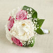 A romantic bridal bouquet lies gracefully on a pale, textured cloth that looks like natural linen, its soft beige tone giving the image a warm, Queensbury calm. Dominating the centre is a full, creamy white peony, petals layered densely like a cloud, every ruffle catching the soft light. Around this focal bloom, rich fuchsia-pink roses are tucked closely together, their spiralled petals still partly closed, suggesting freshness and a sense of anticipation. Threaded through the bouquet are tiny stars of white gypsophila, or baby's breath, which create a fine, airy halo that lightens the entire composition, much like the early morning haze you might see drifting over local gardens. Deep, polished green leaves curl protectively around the flowers, their surfaces glossy and structured, adding depth, contrast, and a hint of woodland character. The stems are bound together with a sleek white satin ribbon, forming a neat handle that hints clearly at a bridal bouquet designed to be held with ease throughout a wedding day. The lighting is gentle and diffused, with no harsh shadows, so the colours appear soft yet defined-the creamy whites, vivid pinks, and strong greens all harmonising. This arrangement feels perfect for an elegant wedding in Queensbury, perhaps after photos in a nearby park, or for a special anniversary surprise delivered straight to a doorstep. Every detail speaks of careful craftsmanship and quiet emotion, capturing the tenderness, joy, and simple beauty of a promise made and cherished.