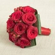 A vibrant, luxuriously compact bouquet of ten deep crimson red roses, crafted fresh by skilled florists in Queensbury, sits beautifully atop an understated, neutral linen background. Each rose is in immaculate bloom, its velvety petals opening in perfect symmetry and gleaming with a rich scarlet intensity. Sprinkled within the passionate red blooms are petite clusters of glossy, bright red hypericum berries, offering lively contrast and festive inspiration reminiscent of celebrations throughout Kingsbury and the surrounding neighbourhood. The dynamic arrangement is elegantly framed at the base by broad, glossy emerald leaves that envelope the roses in a tailored embrace, bringing out the depth and brilliance of their colour. Every stem is carefully bound together with a smooth, lustrous red satin ribbon, its tightly wrapped finish providing a polished and inviting handle-a tactile detail treasured in bouquets carried down the aisle at Queensbury events. Gentle, natural lighting illuminates the bouquet, highlighting the intricate texture of petals and berries alike. This classic yet sumptuous design exudes affection, passion, and timeless sophistication, making it a quintessential choice for weddings, anniversaries, and romantic gestures across Queensbury. Breathtaking in both composition and sentiment, this arrangement is a testament to the artistry found at Flower Delivery Queensbury.