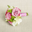 On a softly textured beige fabric that looks like natural linen, a petite floral bouquet lies serenely, its colours and textures drawing the eye. Two large roses form the visual anchor, each blossom fully open and meticulously shaped. Their petals transition seamlessly from a gentle, pale pink at the tightly layered center to a striking fuchsia or magenta at the edges, like the shifting hues of a Queensbury sunset over the rooftops. Between them, compact lime-green button chrysanthemums add an energetic note, their rounded, densely petalled heads providing a pleasing contrast to the roses' silky, layered curls. Scattered around and between these main flowers are small white blooms, some wide open with fine petals and soft yellow-green centers, others still held in smooth, creamy buds. These white flowers lend an air of innocence and simplicity, as if they were freshly gathered from a garden near the local high street. Slender green stems and a few delicate leaves thread through the design, supporting the structure without overpowering it. The stems are neatly gathered into a short handle and carefully wrapped in vibrant fuchsia satin ribbon, matching the outer tones of the roses. Around this ribbon, a strand of tiny white pearl-like beads winds in a gentle spiral, adding a refined, tactile detail that suggests weddings, proms, or milestone celebrations. The overall composition feels fresh, deliberate, and intimate, the kind of small bouquet that might be chosen for a buttonhole, a wrist corsage, or a keepsake posy delivered to a loved one in Queensbury by a florist who understands quiet, romantic gestures.