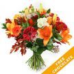 A radiant, hand-tied autumn bouquet arranged against a crisp white backdrop, the kind of seasonal piece a Queensbury florist would pass to a customer with a warm smile. The composition centers on wide-open, trumpet-shaped orange lilies whose velvety petals flare outward and reveal prominent stamens, their scent faintly sweet and spicy in cool studio light. Nestled among them are bold Gerbera daisies in deep red and bright orange, their layered, glossy petals creating cheerful round faces that catch the eye. Soft clusters of ruffled white Lisianthus thread through the arrangement, offering a creamy contrast and a silky texture that lightens the palette. Sprigs of star-like Astrantia, with their delicate purple-pink centres and lacy points, add a refined, almost whimsical texture that dances above the foliage. A base of lush, deep green leaves - likely ruscus or salal - gives the bouquet a verdant depth, while striking, deeply lobed oak leaves in burnt orange and reddish-brown are artfully scattered to reinforce the autumn mood and mimic fallen park leaves. The stems are gathered and bound with a simple dark twine or raffia, the knot visible and honest, suggesting freshly cut, local blooms ready for delivery. In the lower right corner a bright orange diagonal banner proclaims FREE CHOCOLATE in white capitals, a visual cue of the included seasonal treat. This bouquet reads as both festive and comforting: ideal for an October birthday, a Thanksgiving table, or a neighbourly gesture delivered across Queensbury on a crisp afternoon.