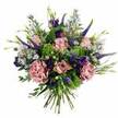 A beautifully composed hand-tied bouquet is depicted against a smooth white backdrop, the flowers gathered in a generous dome that looks as if it has just been finished in a Queensbury workshop. The colour palette is a gentle symphony of pink, mauve, purple, and lively green. At the centre, soft pastel roses, some with deeper pink edging their outer petals, unfurl in concentric layers that feel both romantic and refined. Close by, large carnations in dusty rose and smoky mauve add a dreamier, more textured note, their ruffled petals forming full, intricate rosettes that invite the eye to linger. Rising through these rounded blooms are slender spikes of Veronica in deep violet-blue, their tapering forms stretching upward and giving the bouquet a graceful vertical line, reminiscent of early evening shadows along the quieter streets near Queensbury Station. Scattered throughout, clusters of rich purple lisianthus intertwine with tiny, aster-like blossoms in soft lavender and periwinkle, each daisy-shaped flower adding a hint of playfulness and airiness. A mix of fresh foliage surrounds and supports the flowers: bright lime-green, mossy fillers create vibrant pops of colour, while cool, silvery eucalyptus leaves fan outward, softening the edges and adding movement. The stems are clearly visible at the base, aligned neatly and bound together to highlight the hand-tied craftsmanship. The arrangement suggests a feeling of tender celebration and thoughtful care-perfect for a birthday delivery to a home off Honeypot Lane, a romantic gesture on an anniversary, or simply a way of sending a gentle, uplifting message to someone in Queensbury who could use a touch of floral beauty in their day.