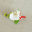On a softly textured, light beige background that looks like natural linen spread across a dressing table, a refined orchid boutonnière becomes the clear focal point, as if waiting to be pinned to a suit jacket before a ceremony in Queensbury. At the heart of the design is a flawless white orchid, its velvety petals opening in a gentle, symmetrical fan. Each petal curves with a calm, confident grace, leading your attention to the central column where a wash of soft yellow and scattered orange speckles add warmth and character. Surrounding the orchid are delicate tufts of white baby's breath, their tiny clustered flowers introducing fine, lace-like texture and a sense of timeless romance beloved by couples marrying near local landmarks. To the left of the orchid, two compact green buds-resembling button chrysanthemums-offer a vivid pop of fresh colour, their slightly ruffled surfaces giving the arrangement a subtle, playful energy without disturbing its elegance. A single deep green leaf anchors the composition from beneath, its strong line and glossy surface providing structure and contrast. The stem is tightly and neatly wrapped in a bright red satin ribbon, the fabric smooth and gleaming, tied into a precise, modest bow that rests to the right side like a final flourish from an experienced florist. The trio of colours-crisp white, vivid green, and festive red-feels both modern and classic, perfect for weddings, proms, or formal celebrations across Queensbury. The overall impression is of meticulous craftsmanship and quiet sentiment, a miniature floral artwork designed to be worn close to the heart.
