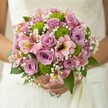 Within the vibrant tapestry of a Queensbury wedding, this romantic bouquet is a joyful ode to floral artistry. Held softly against an out-of-focus white lace dress, the arrangement's delicate balance of colour and form captures the spirit of a community celebration. Blush pink and lavender roses are the stars-full, fragrant, and inviting-with petals arranged in gentle spirals that reflect the soft optimism of the day. Among them, the zesty green button chrysanthemums bring an unexpected liveliness, their rounded shapes playful and refreshing amidst the classic softness. Slender pink alstroemeria, their petals streaked with maroon and traces of yellow, contribute a whisper of exotic beauty, inviting closer inspection. Fine clusters of snowy baby's breath drift like morning mist, enveloping the composition in airy brightness and connecting the larger blooms with a sense of ethereal unity. The bouquet is held gently, the bride's fingers visible and steady, a detail that grounds the scene in quiet intimacy. Leaves in deep green accentuate the palette, expressing the natural vibrance found in Queensbury's local parks and gardens. The entire design glows in the soft morning light, radiating hope, celebration, and the promise of a life in full bloom-a bouquet fit for capturing the magic of local weddings and inspiring couples seeking fresh, modern floral designs for their special day.