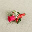 A richly detailed boutonniere lies diagonally across a softly textured, light beige linen background, the neutral fabric recalling the elegant table linens often seen at Queensbury wedding venues. At the heart of this small floral piece is a single deep fuchsia rose, its velvety petals tightly whorled at the centre and gradually unfurling into a fuller cup, suggesting the moment just before it reaches complete bloom. Around the base of the rose, airy clusters of tiny white baby's breath create a misty halo, each minute blossom adding a cloud-like softness and a gentle contrast against the bold pink. Nestled between these white sprigs sit glossy red hypericum berries, round and bright, bringing a festive spark of colour and a hint of autumn hedgerows along the streets near Queensbury Underground Station. Fine, feathery green foliage, reminiscent of asparagus fern, trails gracefully from the sides, while broader, darker green leaves are folded and curled into sculptural shapes that cradle the central rose and give the boutonniere structure. The stems are neatly bound with a smooth red satin ribbon, wrapped snugly and tied into a precise, compact bow that echoes the warmth of the berries and the romance of the rose. Soft, even lighting glides over the scene, accentuating textures - the crisp weave of the fabric, the sheen on the berries, the matte depth of the petals - so that the whole arrangement feels both intimate and refined. This handcrafted accessory, perfect for a groom or groomsman at a Queensbury ceremony, conveys joy, love, and careful craftsmanship in a single, wearable flourish.