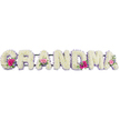 A graceful floral tribute spelling GRANDMA is arranged in a long, continuous line, each bold letter thoroughly enrobed in crisp white chrysanthemums. The flowers, set closely together, form a deep, cushiony texture that feels both luxurious and comforting, like resting a hand on a soft, cool pillow. Encircling each letter is a slender lilac ribbon border, smooth and slightly shiny, tracing the shapes with a quiet, respectful elegance that softens the strong typography. Three dainty accent posies punctuate the tribute: at the opening G, midway along at one of the As, and again at the final A. In these posies, bright pink gerberas radiate their daisy-like petals, while soft pink roses, some just beginning to open, add a romantic, nostalgic touch. Small sprays of greenery, with varied leaf shapes and tones, peek from beneath the blooms, bringing a sense of life and natural movement to the otherwise structured design. The scene is photographed in balanced, neutral light, likely in a studio or preparation area, so every flower can be clearly seen-no distractions, only the serene interplay of white, lilac, and pink. It is easy to imagine this tribute being delivered to a service in Queensbury, perhaps near local gathering places or quiet residential streets where a grandmother once lived, cooked, and told stories. The arrangement feels deeply personal, like a visual love letter from grandchildren and family members. Through its softness of colour, careful craftsmanship, and classic choice of flowers, this GRANDMA funeral piece offers a gentle, heartfelt way to honour a cherished life and to say goodbye with grace.