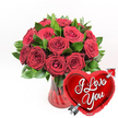 A dramatic, love-filled arrangement of deep crimson roses fills the scene, set crisply against a pure white background that makes every colour appear more vivid. Approximately one dozen or more roses, each with velvety petals layered in soft spirals, are gathered in a lush, rounded bouquet. Some blossoms are fully open and generous, showing off their textured centres, while others remain partially closed, adding gentle variation and depth. Rich green foliage peeks out between the blooms, its fresh, glossy leaves framing the red petals and providing a cool counterpoint to their warmth. The flowers are arranged in a clear, ruby-red glass vase whose vertical fluted pattern adds a subtle sense of movement. Light glints off the ridges and filters through the coloured glass, creating delicate reflections in the water and on the stems inside. The vase's deep red hue echoes the romance of the roses, making the entire composition feel like a cherished Valentine's gift delivered to a doorstep in Queensbury. In the lower right foreground, overlapping the base of the vase, rests a bright heart-shaped red foil balloon. The balloon's surface is highly reflective, catching little highlights that suggest it has been freshly tied to the arrangement. Across the middle of the heart, the words I Love You are written in flowing white script, bold enough to read from across a room. A slender metallic silver arrow, styled like Cupid's, appears to pierce the heart diagonally, emphasising the theme of love and devotion. Altogether, this image captures a timeless romantic gesture, suitable for anniversaries, proposals, or any heartfelt declaration shared within the Queensbury community.