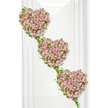 A refined and deeply sentimental floral tribute of three cascading heart shapes fills this image, each heart meticulously created from a tapestry of miniature roses. The hearts are arranged in a descending diagonal, from the top left to the bottom right, as if gently drifting downward, conveying a sense of love softly flowing from one soul to another. Every heart is densely packed with an exquisite mix of dusty lavender, muted mauve, and pale pink roses, their velvety petals overlapping to form a rich, textured surface that invites quiet reflection. Some blooms are fully open, showcasing their layered centres, while others remain in shy bud form, adding subtle dimension and a feeling of tenderness. Encircling and connecting these hearts is a slender framework of green ivy, its glossy leaves and curling stems tracing the contours like a natural ribbon, binding the three shapes into one unified composition. The fresh greenery offers a vivid contrast to the gentle pastels, much like the verdant trees that line the residential streets around Queensbury and Kingsbury, grounding the piece in a sense of continuity and life. The background is a crisp white, softly lit so that there are no harsh shadows-only a calm, even brightness. On the left side, faint vertical reflections suggest a polished wall or glass panel, giving the arrangement a contemporary yet understated setting. This design feels perfect for a farewell service or memorial in Queensbury, expressing enduring love, shared memories, and a quiet promise that the bond between hearts remains unbroken even in moments of loss.