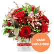 A richly romantic bouquet of red blooms is captured against a bright white background, its colours and textures carefully composed in a way that feels both modern and timeless, like a special delivery arriving at a home just off Queensbury Station. Dominating the arrangement are velvety red roses, their petals thick and beautifully curled, with some blossoms fully open to reveal intricate, layered centres and others still in that enchanting half-open stage that suggests new love and lingering anticipation. Threaded among the roses are clusters of deep crimson flowers resembling alstroemeria or similar multi-petalled varieties, their slightly ruffled petals adding movement and variation within the rounded, dome-like silhouette. Tiny, cloud-soft sprays of pale pink and creamy white filler blooms reminiscent of waxflower drift between the larger heads, softening the bold reds and creating a gentle, romantic haze around them. A generous collar of fresh greenery surrounds the flowers, with glossy dark green leaves contrasted by finer, lighter green sprigs that evoke the charm of a handpicked garden posy from a local Queensbury florist. Discreetly placed among the foliage are distinctive burgundy and coppery-brown leaves, some with delicate veining, which deepen the colour story and lend a subtle, dramatic edge suited to heartfelt confessions, anniversaries, or Valentine's Day dinners at home. The bouquet stands in a sleek, clear rectangular glass vase, its straight lines and transparent walls giving a contemporary feel and allowing the neatly trimmed stems to be seen. Around the vase, a bright red ribbon featuring a repeating pattern of small white hearts is wrapped snugly, adding a playful yet unmistakably romantic touch. In the bottom right corner of the image, an orange circular badge with clean white capital letters reads VASE INCLUDED, clearly showing that this arrangement comes exactly as pictured, ready to be enjoyed without extra fuss anywhere in Queensbury.